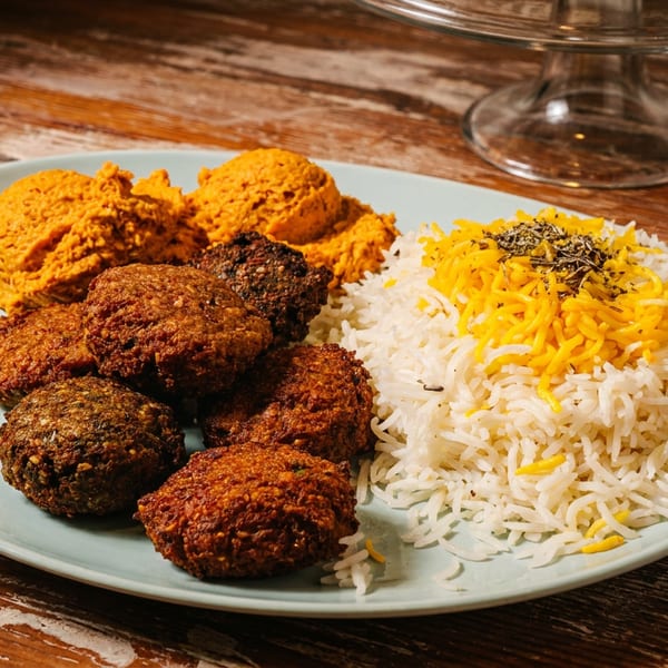 A plate of falafel, orange hummus, and white rice with yellow saffron strands and herbs.