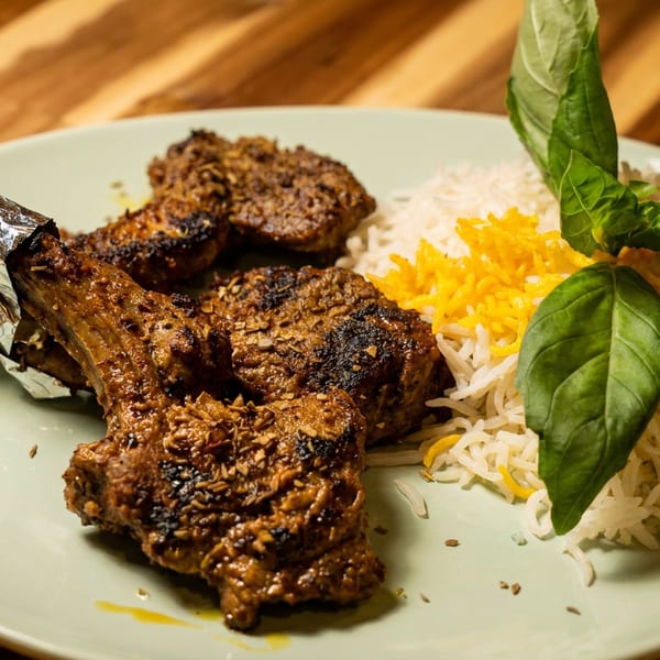 Grilled lamb chops with rice, saffron, and basil on a light green plate.