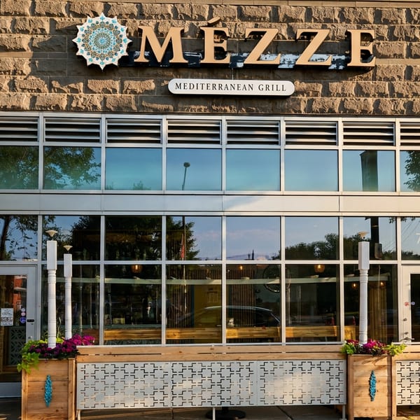 Exterior of Mezze Mediterranean Grill, a restaurant with large windows and outdoor planters.