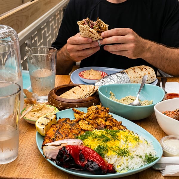 A person eating a wrap at a table filled with various Middle Eastern dishes and drinks.